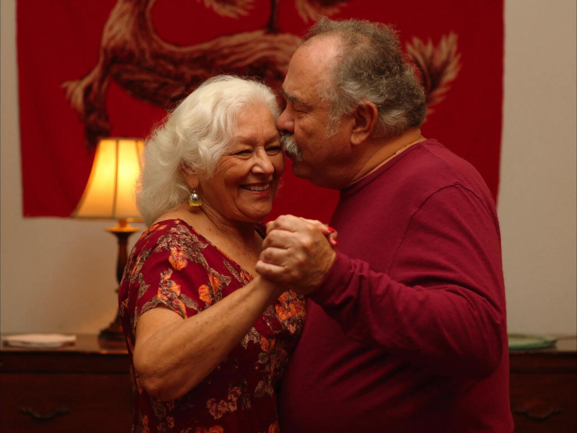 Casal idoso brasileiro dançando lentamente na sala com luz dourada